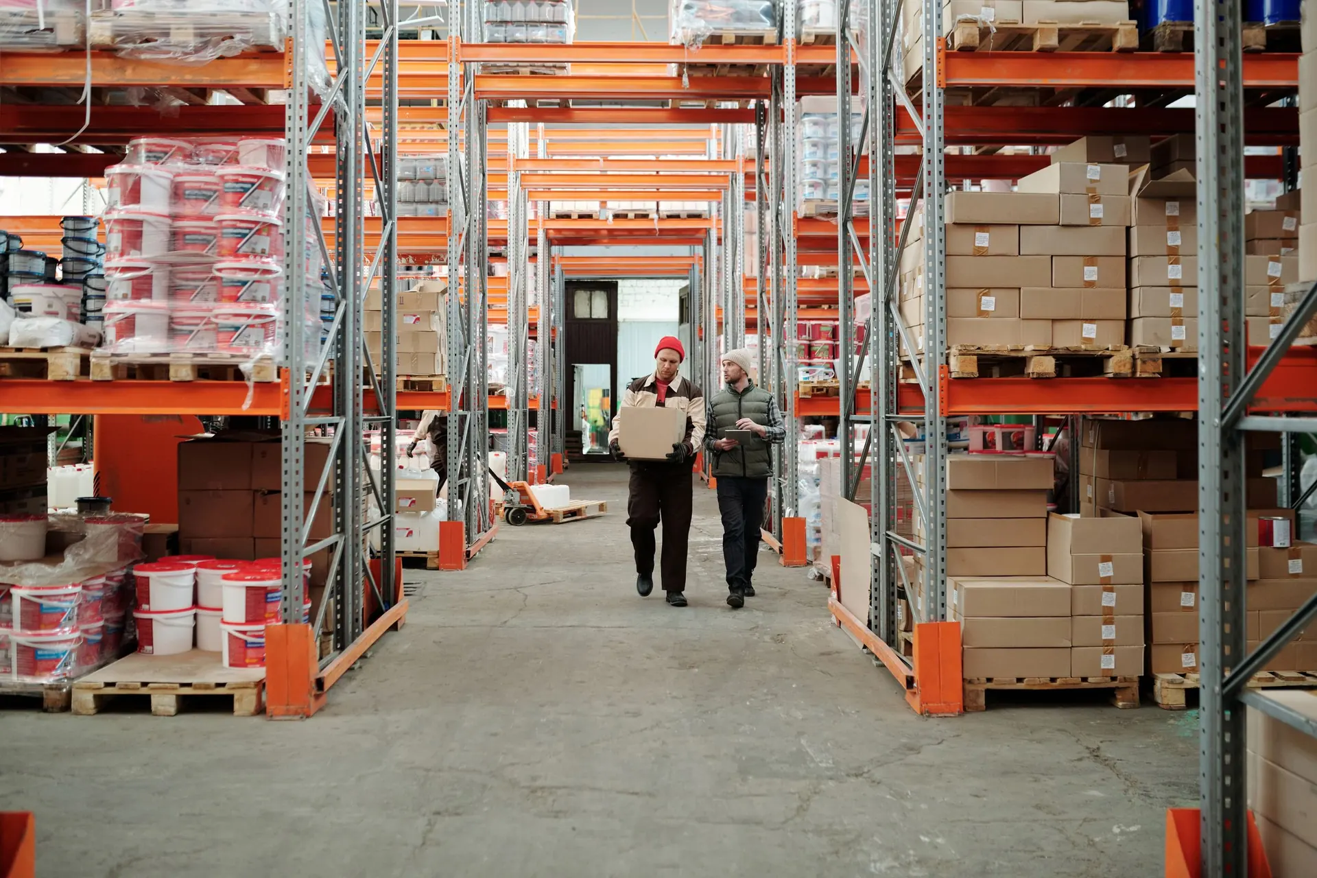Warehouse staff walking along a stocked pallet-racking aisle