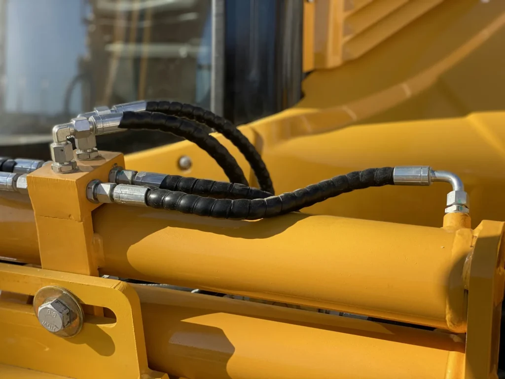 Close-up of a crimped hydraulic hose fitted to a yellow heavy-equipment cylinder